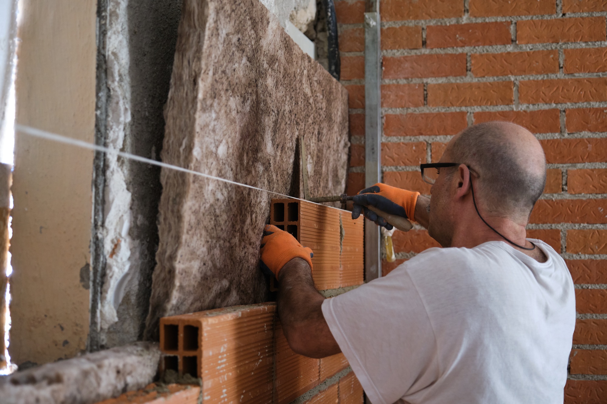 Builder laying bricks after placing an acoustic and thermal insulation.